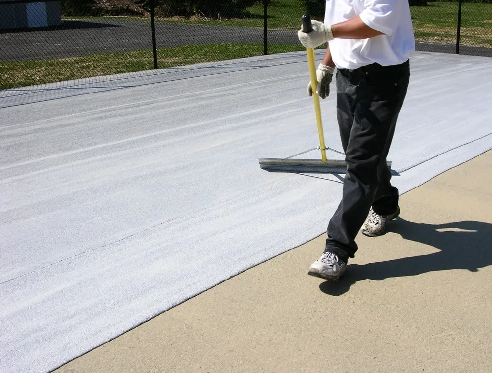 Professional court contractor applying textured acrylic coating with a flexible rubber squeegee